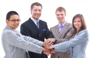 Teamwork and team spirit - Hands piled on top of one another with a multi-ethnic group in the background